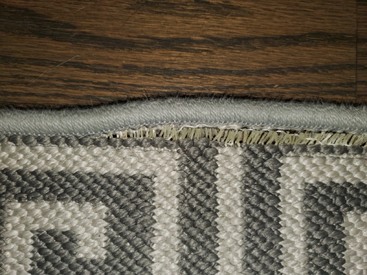 Tufted carpet edge where serging unraveled because the backing wasn&rsquo;t latex-coated before cutting