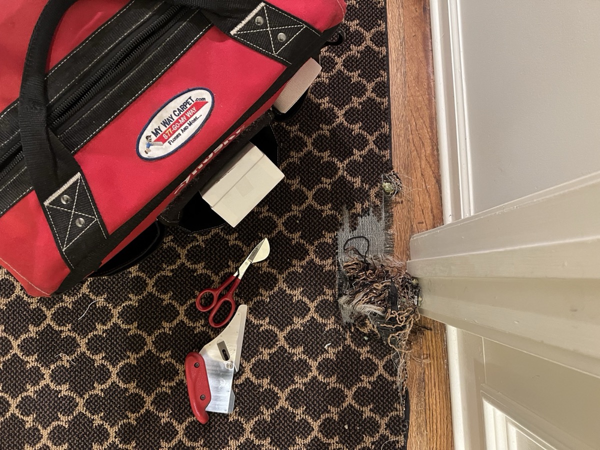 Damaged binding at a hallway doorway, with My Way Carpet tools staged next to the frayed edge